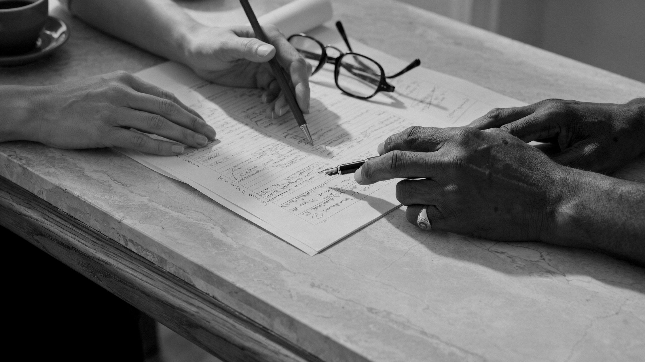 An experienced practitioner and a manager working over the same annotated document, in black and white